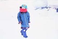 [Young Inuk child wearing a "CAT" baseball hat and a thick red scarf walking in the snow, Western Arctic (Inuvialuit)]
