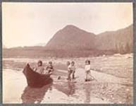 [Three Indigenous children playing with a toy canoe, while two other children watch from a nearby canoe]. Original title: Indian Children [between 1900-1910].