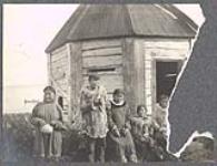 [Yup'ik man and women standing in front of conical building in Taciq (St. Michael)] [between 1889-1942].