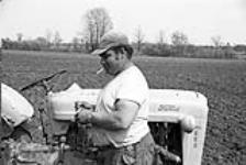 [Councillor Cedrick Marable, Kanien'keha:ka (Mohawk) from Tyendinaga, lighting a cigarette beside a tractor] [ca. 1959]