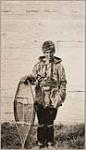 [Anishinaabe man, Laxdywar Nimar dressed in fur hat, fringed hide jacket, mittens, and leggings. He is holding snowshoes] [ca. 1916]