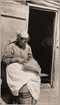 [Anishinaabe woman, identified as Mrs. Gotcr, is seated and sewing a birch bark basket] [ca. 1916].