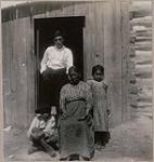[Katie Gibson and three orphans in front of a wooden house] 1912