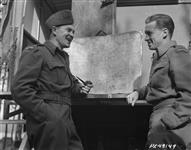 Operating from the same "summer resort" airfield as fighter wing, RCAF recce wing, commanded by G/C George H. Sellers, of WINNIPEG (104 Grenfell Blvd.) Left, seen chatting with his wince ops, W/C R.S.A. "Hunt" Waddell, DFC, of Peterborough Ont. (Menaghan Rd) on the folding "verandah" of C.O. van. Serving as combined office and sleeping quarters, van is tucked away in pine grove like a trailer at a tourist camp April 5, 1945.