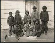 [Group of Tlicho children posing in front of building]. Original title: Group of Dog Ribbed Indians, Great Slave Lake [ca. 1901].