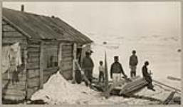 [Unidentified woman in the doorway of a house with unidentified men outside and an unidentified young boy sitting on a Kamutik] [between 1921-1922]