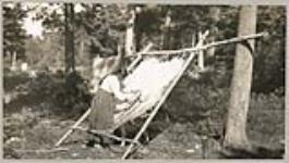[Anishinaabe woman scraping a moose hide hung on a frame] 1919.