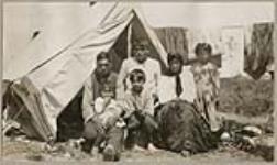 [Anishinaabe family seated outside in front of a tent] 1920