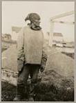 [Innu man, Johnny, at Nain dressed in fur-trimmed parka, mittens, boots, and bandana] [between 1921-1922]