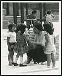 [Woman (possibly a teacher) interacting with a group of small children] [ca. 1960-1970]