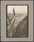 Man standing on cliff overlooking ocean [ca. 1930].