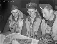 Target was Sterkrade, a strategic industrial town in the Ruhr, and the Nazis defended it vigorously with flak batteries and night-fighters. The Iroquois Squadron [431 Squadron] trio pictured above are telling an intelligence officer how they saw the objective pranged. Shown are (left to right) P/O Hal. Phillips (2127 W. 40th St., Vancouver); F/O Gordon Dumville (Rocanville, Saskatchewan); F/O R. W. Harrison (Lorlie, Saskatchewan). All have done more than ten trips with the RCAF Bomber Group 17 June 1944.