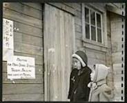 Two young Japanese girls pause for a glance at the signs outside the camp school [1943/11-1943/12]