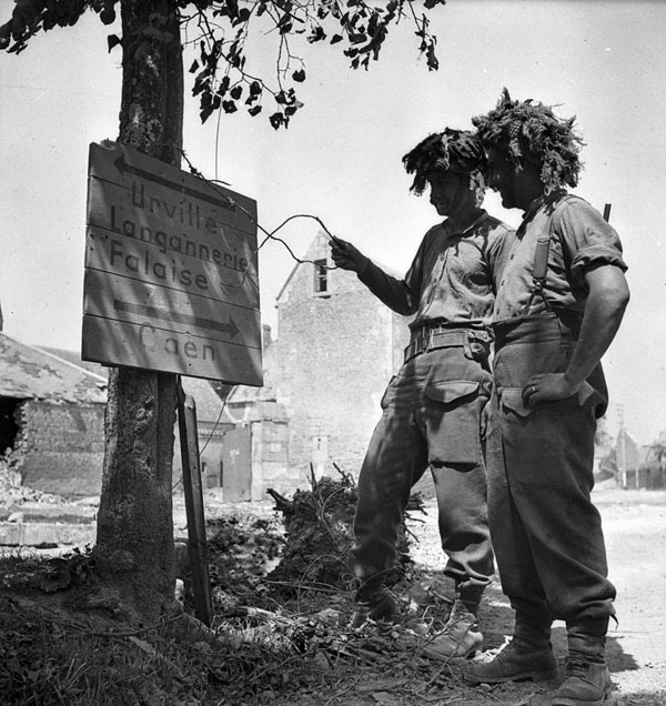 Troopers J.L. Gaudet and G.A. Scott of The South Alberta Regiment pause in front of a sign pointing towards Falaise. Cintheaux, France, 9 August 1944.