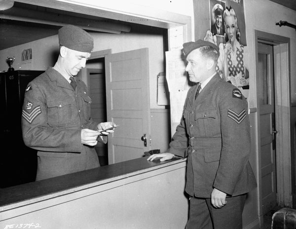 An unidentified flight-sergeant checking the pass of an unidentified corporal at the guardhouse of Royal Canadian Air Force Station Rockcliffe, Ontario, Canada, 26 April 1944.