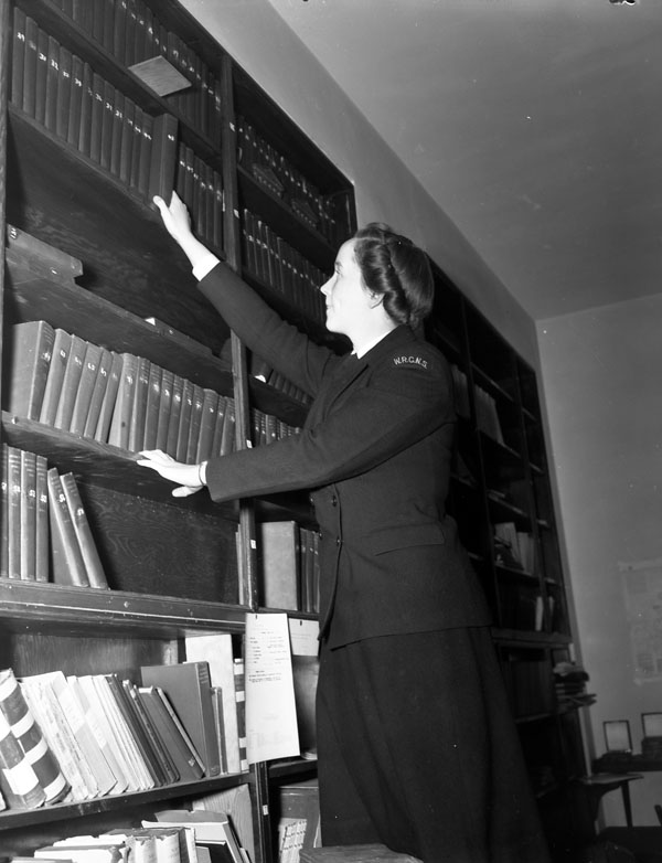 Wren Writer M. McDonald of the Women's Royal Canadian Naval Service (W.R.C.N.S.) arranging navigation books in the library at H.M.C.S. KINGS, Halifax, Nova Scotia, Canada, 3 March 1943.