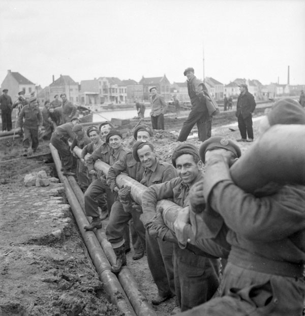 Personnel of the 3rd Battalion, Royal Canadian Engineers (R.C.E.) lowering a section of the Ostend-Ghent oil pipeline into a trench, Ostend, Belgium, 18 October 1944.