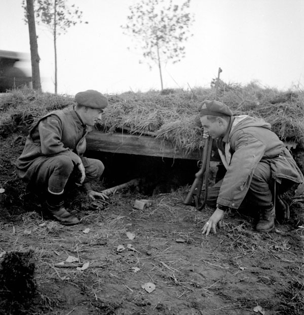Sergeants M.J. Gendron and R.L. O'Hara of the Royal Canadian Corps of Signals (R.C.C.S.), 2nd Canadian Infantry Division, examining a concealed German anti-tank gun position on the Beveland Causeway, Netherlands, 27 October 1944.