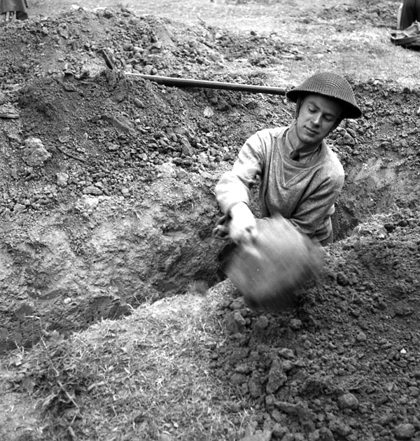 Lieutenant Ken Bell of the Canadian Army Film and Photo Unit digging a slit trench in the Normandy beachhead, France, 10 June 1944.
