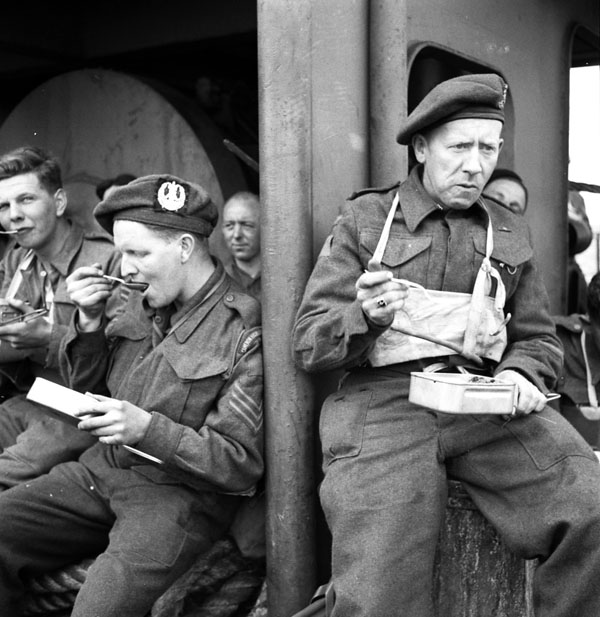 Canadian infantrymen from various units, including The Cameron Highlanders of Ottawa (M.G.), eating a meal aboard ship en route to the Normandy beachhead, France, 6 June 1944.