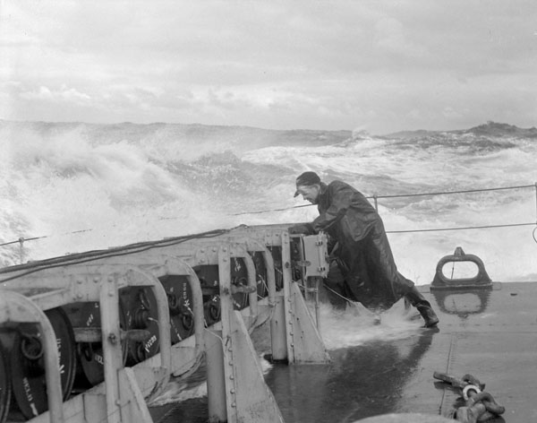 An unidentified sailor checking the stowage of depth charges at the stern of the frigate HMCS Matane in heavy seas off Bermuda.