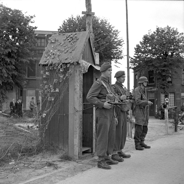 Privates W.R. Hill and M.A. Gammon of 1st Canadian Corps on guard duty with a German soldier, also on guard duty, at the German garrison, Ijmeuden, Netherlands, 11 May 1945.
