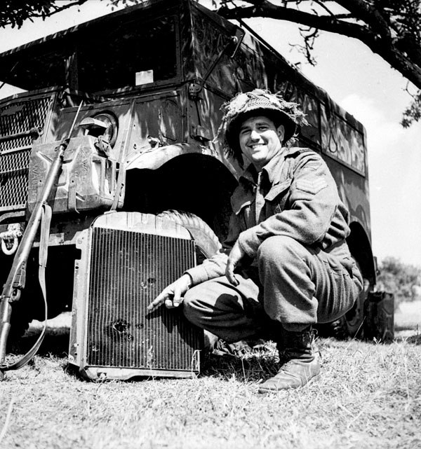 Sergeant R.A. Garbutt of the 19th Field Regiment, Royal Canadian Artillery (R.C.A.), showing shrapnel holes in the radiator of his vehicle made by a German 88mm. anti-tank gun in Normandy, France, 16 June 1944.