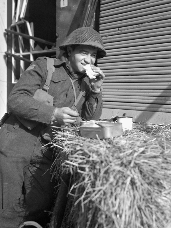 Lance-Corporal W.D. Bunka of the Anti-Tank Platoon, Royal Winnipeg Rifles, eating a meal on a bale of straw, Ijzendijke, Netherlands, 21 October 1944.