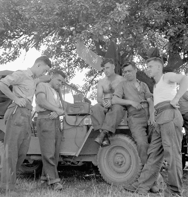 Personnel of Rear Headquarters, 2nd Canadian Infantry Division, listening to the British Broadcasting Corporation (B.B.C.) news from London. Laize-la-Ville, France, 12 August 1944.