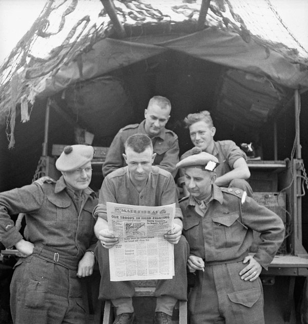 Infantrymen of the Toronto Scottish Regiment  (M.G.) reading the first issue of the Maple Leaf newspaper between Fleury-sur-Orne and Ifs, France, 28 July 1944. (Front, L-R): Captain Jack Crawford, Sergeant Clarence Rowllinson, Lieutenant John Farnan. (Rear, L-R): Privates Garry Vachon and Phil Jackson between Fleury-sur-Orne and Ifs, France.