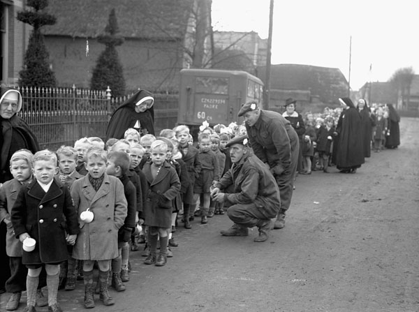 Private M.M. Barnhart and Lance-Corporal C.G. Balazs talking with children attending a Christmas party sponsored by the Argyll and Sutherland Highlanders of Canada, Elshout, Netherlands, 17 December 1944.