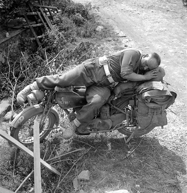 Lance-Corporal Bill Baggott sleeping on his motorcycle, Falaise, France, ca.13-14 August 1944.