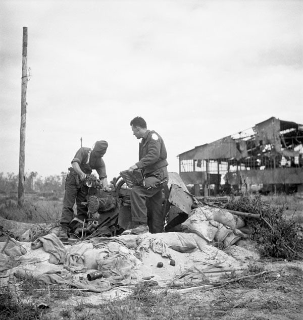 Sergeant N.E. Theriault and Lance-Corporal E.G. Chassie examining a damaged German anti-aircraft gun on the airfield at Carpiquet, France, 12 July 1944.