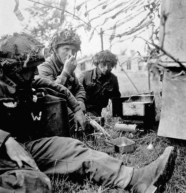 Infantrymen of the 7th Canadian Infantry Brigade cooking supper in a camouflaged hut, Authie, France, 9 July 1944.