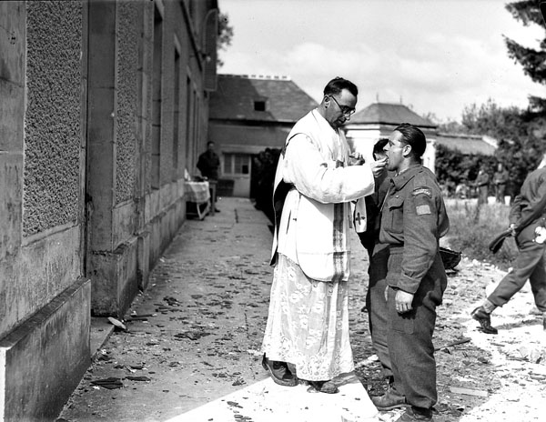 H/Captain Wilfrid Huard administering Holy Communion to infantrymen of 