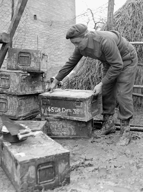 Gunner Russ Kannett of the Royal Canadian Artillery (R.C.A.) selecting a 4.5-inch shell charge case to be converted into a stove, Ravenna, Italy, 10 February 1945.