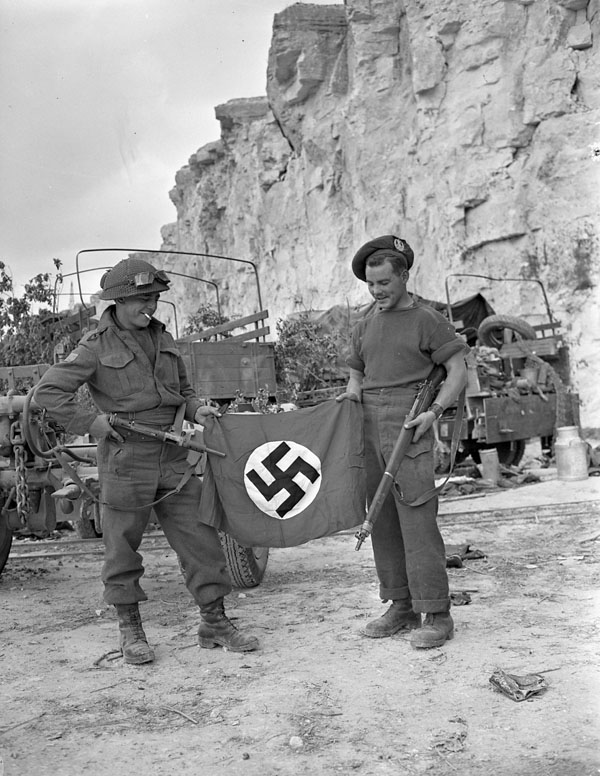 Privates L.B. Roy and R.L. Parker, Cameron Highlanders of Ottawa, with a German flag captured in a quarry south of Hautmesnil, France, 10 August 1944.