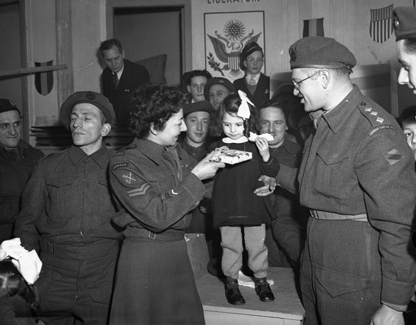 Corporal M. Freeman, Canadian Women's Army Corps (C.W.A.C.), and H/Captain Samuel Cass, Jewish chaplain, presenting a gift to a Belgian girl during a Hanukkah celebration, Tilberg, Netherlands, 17 December 1944.