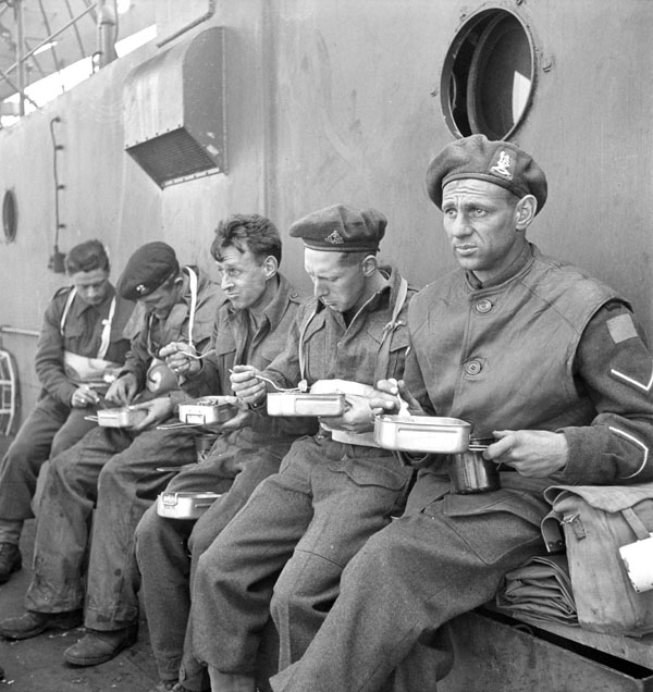 Soldiers of the 9th Canadian Infantry Brigade eating aboard a landing craft en route to France, 6 June 1944.