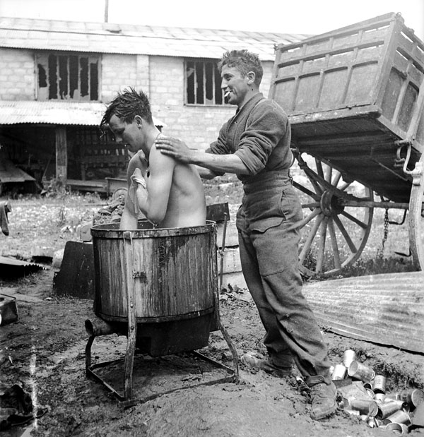 Rifleman  E. Deblois, Queen's Own Rifles of Canada, washing the back of Rifleman J.C. Sackfield of the same regiment, who is having a bath, Bretteville-Orgueilleuse, France, 20 June 1944.