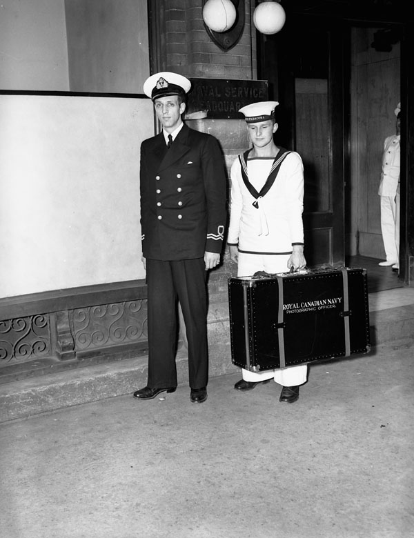 Lieutenant Alfred O. Tate, an official Royal Canadian Navy photographer, and his assistant, who carries a case of photographic equipment, Ottawa, Ontario, Canada, 11 July 1940.