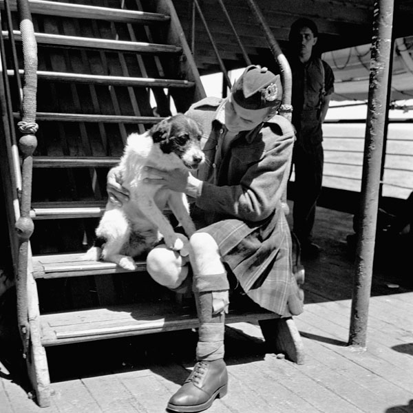 Private Peter Bross, and mascot Bob, of a Canadian Highland regiment aboard the troopship H.M.T. NEA HELLAS en route to Philippeville, Algeria, 8 July 1943.