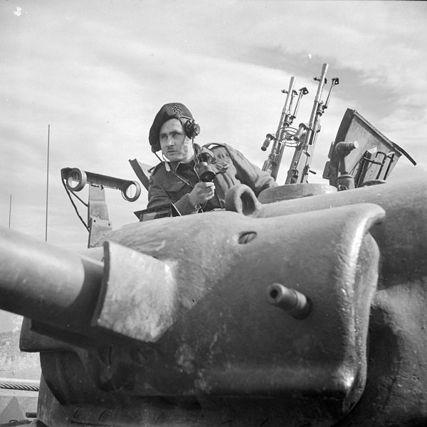 An unidentified crew commander of the 8th Princess Louise's (New Brunswick) Hussars in the hatch of his Sherman tank giving firing orders to his gunner during a predicted mass tank firing exercise, Italy, 2 March 1944.