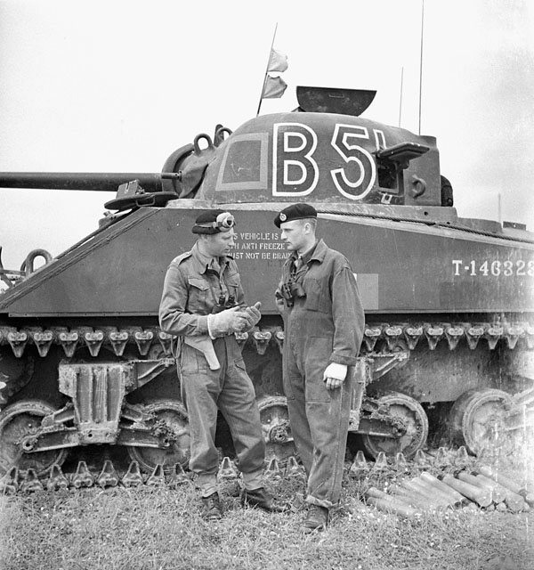 Unidentified crewmen standing next to their Sherman tank during a lull in a combined armour and artillery exercise, England, 5-10 June 1943.