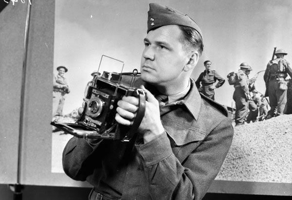 Lieutenant Jack H. Smith of the Canadian Army Film and Photo Unit, who is holding a Graflex Speed Graphic press camera, London, England, ca. 1941-1942.